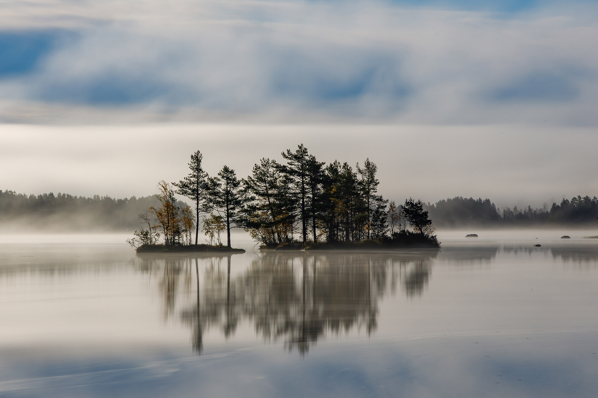 Foggy island in a calm lake surrounded by Nordic nature